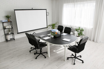 Interior of conference hall with table, shelving unit and projector screen in modern office