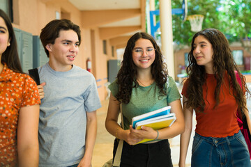 Group of cheerful high school students walking and talking in school hallway