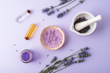 Lavender bath salt in a bowl, mortar and pestel with lavender flowers, aroma oil and hydrolat on purple background. Natural herbs medicine, aromatherapy concept. Top view, flat lay