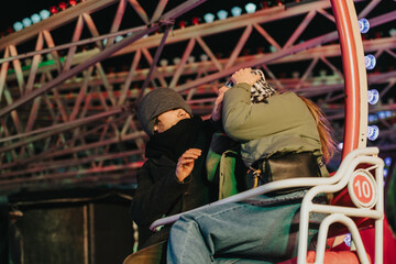Two individuals seated on a ferris wheel, sharing a joyful moment against a night-lit amusement park backdrop. Colorful lights and mechanical structures add to the whimsical and lively atmosphere.