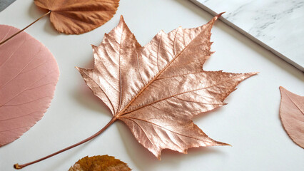 Artistic arrangement of copper and pink painted autumn leaves on a white surface
