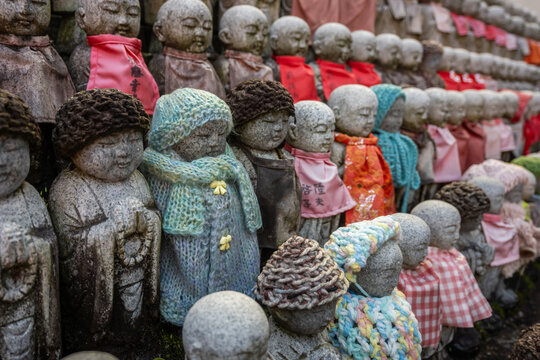 Stone Jizo statues, guardians of children, in Osaka, Japan, wear colorful knitted red hats and red bibs. A tradition offering protection and blessings.