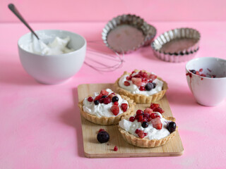 Yogurt and red fruit tartlets accompanied by ingredients and kitchen utensils. Pastel pink...