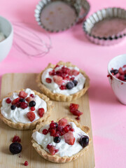 Yogurt and red fruit tartlets accompanied by ingredients and kitchen utensils. Pastel pink background. Cool and colorful atmosphere
