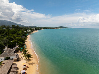 Tropical sandy beach with turquoise sea and palm trees along the shore under a bright sky. Koh Samui, Thailand.