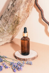 Amber serum bottle on wooden stand and lavender flowers in sunlight. closeup