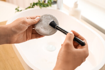 Female hands washing makeup brush with tool over sink in bathroom, closeup