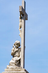 Statue of an angel holding a cross and praying at the feet of the crucified Christ. Blue sky. São João Batista Cemetery, Rio de Janeiro, Brazil