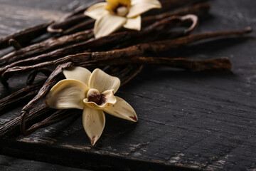 Vanilla sticks and flowers on dark wooden background, closeup