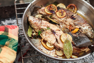 Grilling vegetables, sausages, and trout over charcoal in a backyard during summer. Outdoor cooking with real flames and smoke in a cozy home setting