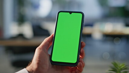 Man hand holding green screen mobile phone having video call in office closeup. 