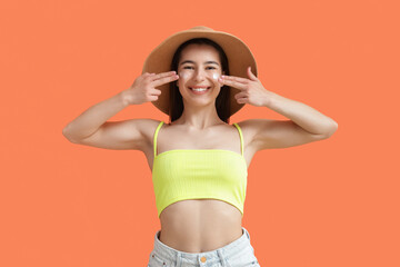 Young woman in hat applying sunscreen cream on orange background