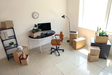 Interior of office with workplace, shelf unit and cardboard boxes on moving day