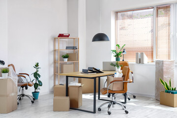 Interior of office with workplace, plants and cardboard boxes on moving day