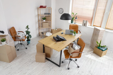 Interior of office with workplace, plants and cardboard boxes on moving day