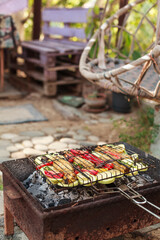 Grilling vegetables, sausages, and trout over charcoal in a backyard during summer. Outdoor cooking with real flames and smoke in a cozy home setting