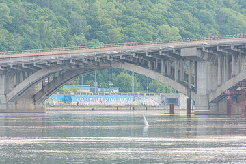 Overcast day in Kiev Tranquil Dnepr River crossed by arched bridge with intricate cable and support...