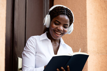 Young African female student reading book in front of the college and relaxing.