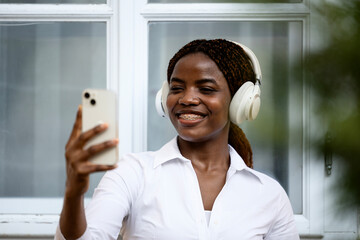 Positive black girl taking self-portrait photograph while listening to music.