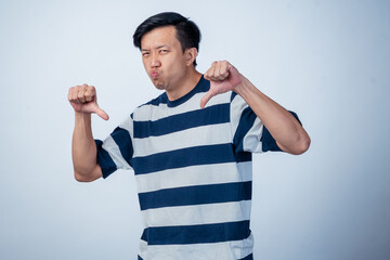 Asian man in striped shirt making a double thumbs-down gesture with a displeased facial expression,...