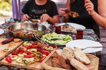 Grilling vegetables, sausages, and trout over charcoal in a backyard during summer. Outdoor cooking with real flames and smoke in a cozy home setting