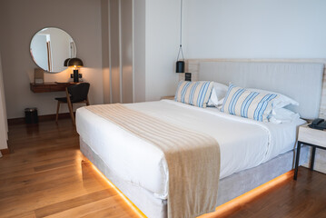 A stylish hotel room featuring a double bed with striped pillows, beige throw, wooden flooring,...