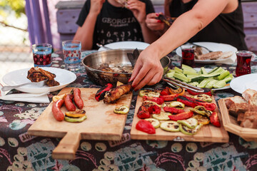 Grilling vegetables, sausages, and trout over charcoal in a backyard during summer. Outdoor cooking with real flames and smoke in a cozy home setting
