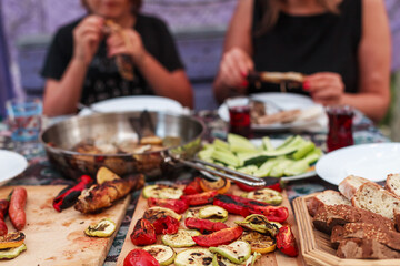 Grilling vegetables, sausages, and trout over charcoal in a backyard during summer. Outdoor cooking with real flames and smoke in a cozy home setting