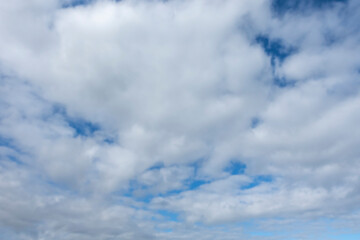 A serene view of fluffy white clouds scattered across a vibrant blue sky, creating a peaceful and...