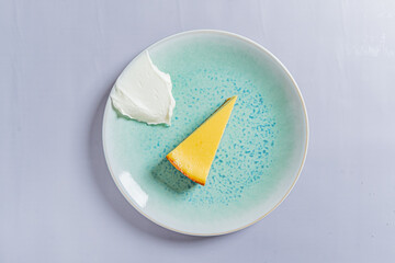 A bright yellow slice of cheesecake rests on a turquoise plate, complemented by creamy topping