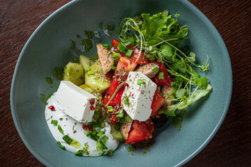 A colorful bowl filled with fresh salad greens, tomatoes, cucumbers, and creamy feta cheese