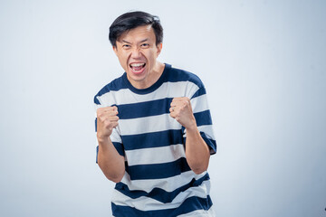 Asian man in striped shirt celebrating with clenched fists and joyful expression, showing...
