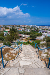 A stone staircase with blue railings descends towards a coastal town in Cyprus, featuring...