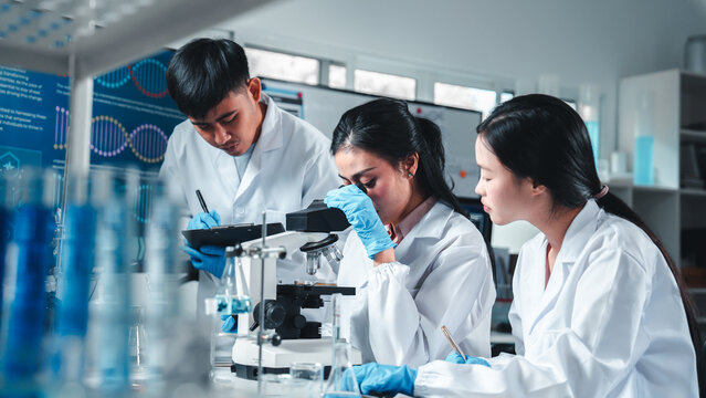 A group of young scientists work together in a laboratory, focused on using a microscope and recording observations. The scene shows teamwork, research analysis, and scientific documentation. - Powered by Adobe