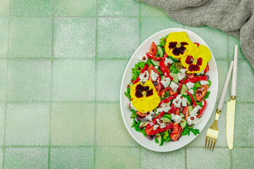 Fresh vegan salad with tomatoes, arugula, goat cheese, olives, and edible flowers on a white plate