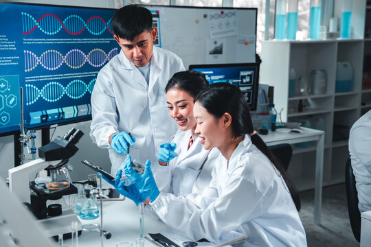 Young researchers collaborate in a high-tech lab, smiling and discussing data on a digital tablet. Surrounded by lab tools and digital screens, they represent teamwork, diversity, and innovation.