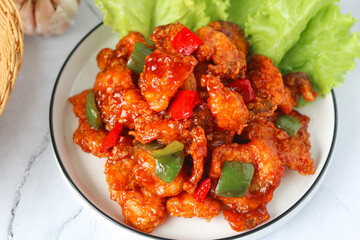 Top view of homemade sweet and sour fish with bell peppers, served on a white plate with fresh lettuce on the side. Captured with natural light on marble background.