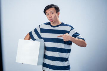 Asian man in striped shirt smiling and posing with one hand resting on a large white cube, standing against a plain light blue studio background