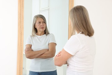 Beautiful senior woman looking at herself in mirror indoors