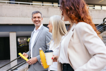 Businesspeople walking outside office holding reusable coffee cup and water bottle, discussing artificial intelligence and contracts