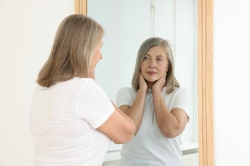 Fototapeta premium Beautiful senior woman looking at herself in mirror indoors