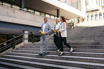 Businesspeople are walking down the stairs of their office building while discussing a new contract
