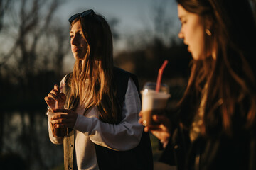 Girls spending time outdoors, sipping beverages and enjoying the tranquility of the sunset, with a...
