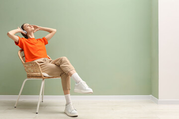 Beautiful woman with headphones relaxing in comfortable wicker armchair near pale green wall...