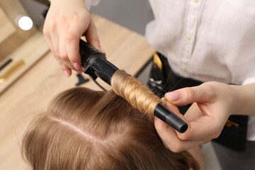 Naklejka premium Hairdresser curling woman's hair in salon, closeup