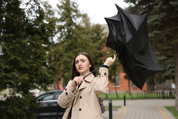 Woman with broken umbrella fighting wind outdoors