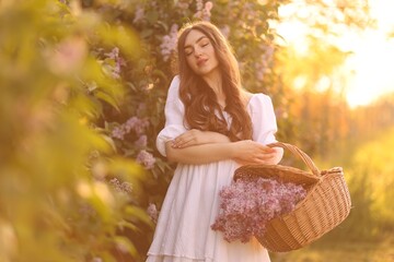 Beautiful woman with basket of lilac flowers outdoors in morning