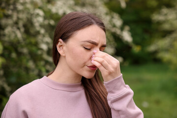 Woman suffering from seasonal pollen allergy near blossoming shrub on spring day