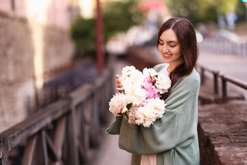 Fototapeta premium Charming woman with bouquet of beautiful peonies on city street. Space for text