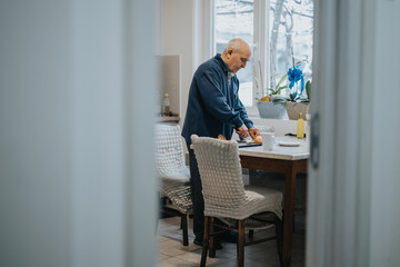 A senior man is slicing vegetables on a countertop in a cozy kitchen adorned with plants and...